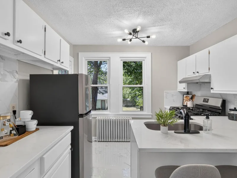 Kitchen with white cabinetry, stone counters and a window above the radiator