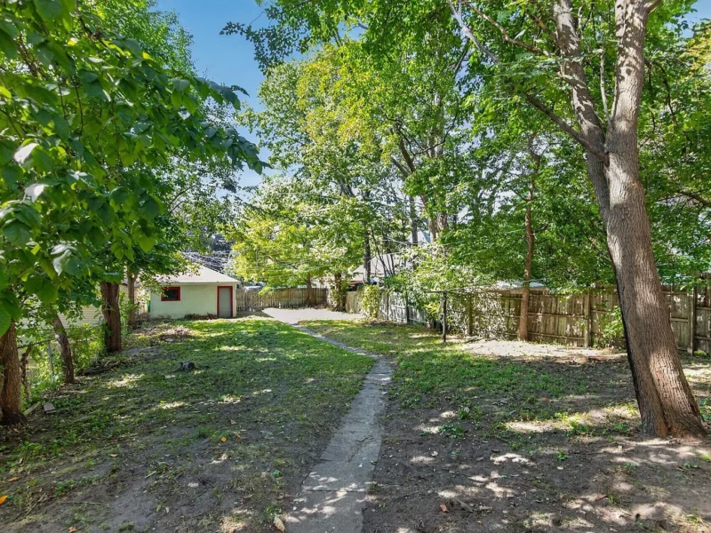 Grassy yard with mature trees and a path toward the alley