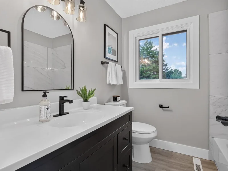 Bathroom with a black vanity, white countertop and arched mirror