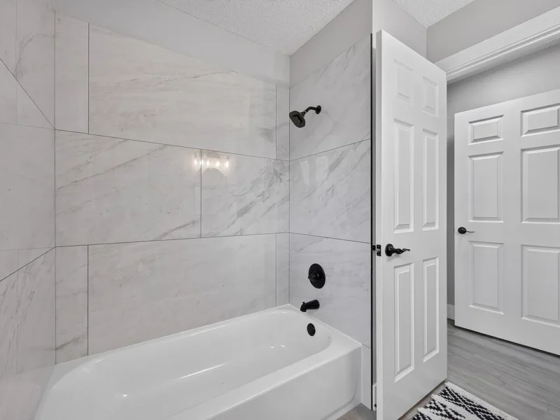 Bathtub with a large-format white tile surround and black fixtures